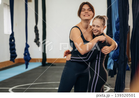 Embracing each other. Female instructor helping a child practice aerial yoga on hammock straps in a fitness studio 139320501