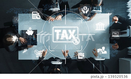 Aerial view of a business meeting with tax icons and charts on a table. Professionals engage in financial discussions, emphasizing planning and strategy around taxation and finances. Sigmoid 139320536
