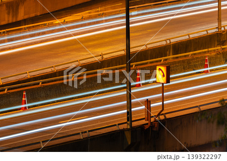Long exposure night traffic creating light trails on highway with road sign and cones urban transport motion speed infrastructure and safety guidance 139322297