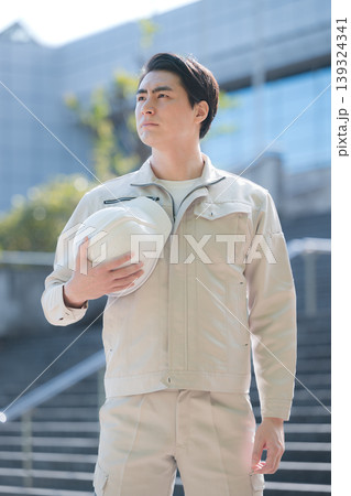 ヘルメットを持つ若手作業員のポートレート 建設現場と成長、ビル背景に未来や希望を見つめる、見上げる ヘルメットを持つ若手作業員のポートレート 建設現場と成長、ビル背景に未来や希望を見つめる、見上げる 139324341