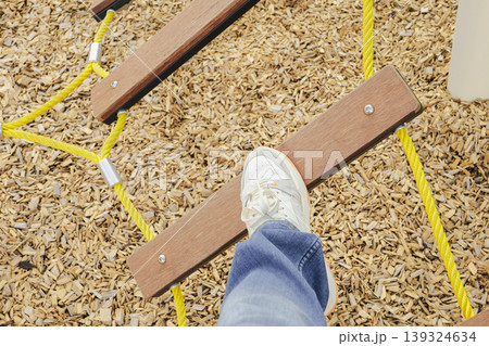 Person balancing on wooden plank bridge in a playground. Joy of simple challenges. 139324634
