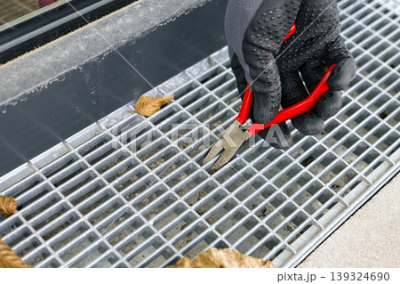 Maintenance task of a metal terrace drain grate, highlighting practical outdoor repair and routine upkeep. Maintenance task of a metal terrace drain grate, highlighting practical outdoor repair and routine upkeep. 139324690