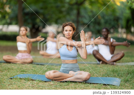 Multinational yoga enthusiasts with female coach perform padmasana in park Multinational yoga enthusiasts with female coach perform padmasana in park 139324900