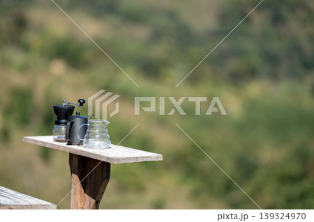 The coffee grinder, kettle, and coffee pot arranged on the table at the beautiful flower field view above the forest and mountains background The coffee grinder, kettle, and coffee pot arranged on the table at the beautiful flower field view above the forest and mountains background 139324970
