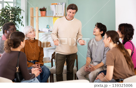 Positive man standing communicating with group of adult people at seminar in advanced training Positive man standing communicating with group of adult people at seminar in advanced training 139325006