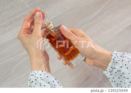 Woman holds perfume bottle, gently twisting cap Woman holds perfume bottle, gently twisting cap 139325049