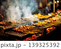Grilling satay skewers over charcoal with flames at an outdoor cooking station. 139325392