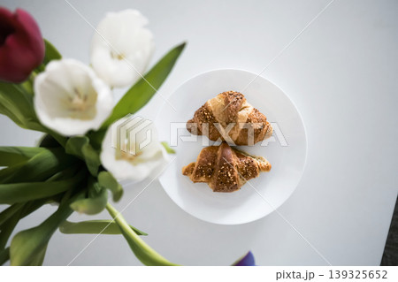 Tho croissants on a plate with white and red tulips in the foreground 139325652