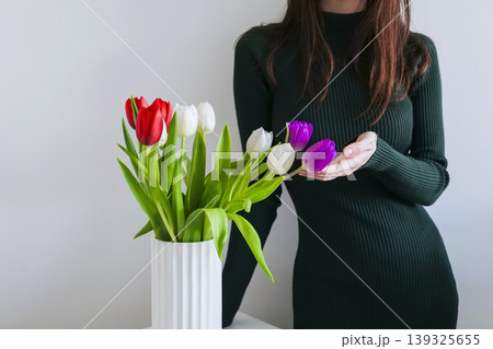 Woman in an elegant green dress stands next to a vase with multi-colored tulips on a white background 139325655