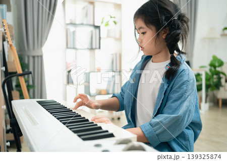 Young girl practicing piano at home, focused and creative, exploring music and rhythm, developing skills in modern and cozy environment Young girl practicing piano at home, focused and creative, exploring music and rhythm, developing skills in modern and cozy environment 139325874