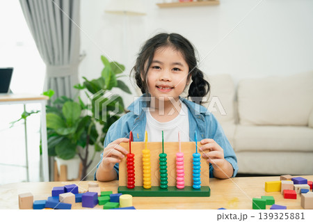 Happy girl learning with colorful counting beads at a table in a bright and cheerful playroom filled with toys and plants for educational activities Happy girl learning with colorful counting beads at a table in a bright and cheerful playroom filled with toys and plants for educational activities 139325881