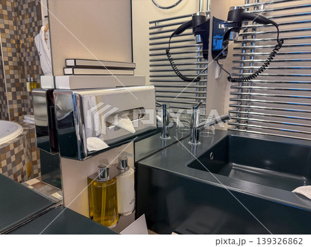 Hotel room bathroom with sink, mirror, hair dryer, toiletries in modern interior setting. Hospitality service, travel accommodation, guest comfort, hygiene concept, hotel amenity 139326862