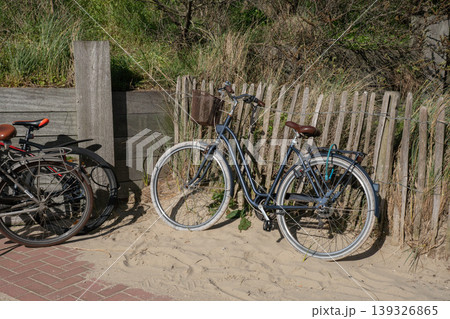 Bicycles parked on sandy beach near wooden fence, dune grass under natural daylight. Urban mobility, eco transport, outdoor lifestyle, coastal travel, sustainable transportation content Bicycles parked on sandy beach near wooden fence, dune grass under natural daylight. Urban mobility, eco transport, outdoor lifestyle, coastal travel, sustainable transportation content 139326865