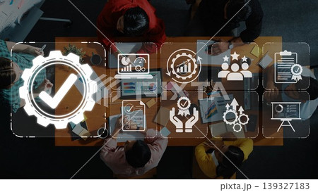 Aerial view of a diverse team discussing strategies around a table with laptops and documents. Business icons highlight themes of collaboration, growth, and success in the workspace. Sigmoid 139327183