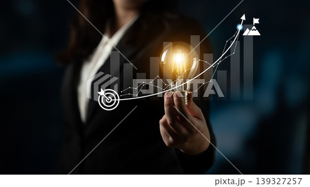 Business concept of innovation and growth represented by a light bulb in hand with graphs indicating progress in a dark corporate setting Ledger 139327257