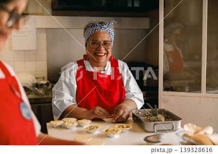 Happy senior woman smiling while preparing homemade tarts in professional kitchen 139328616