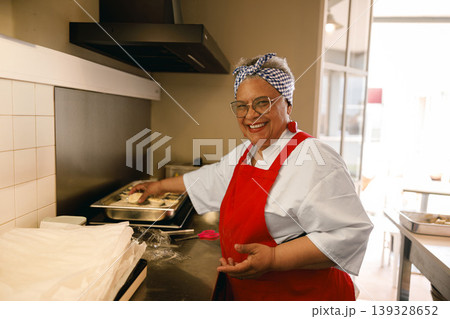 Happy senior woman in red apron standing in kitchen while preparing food 139328652