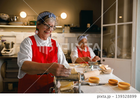Senior Caucasian Woman Making Fresh Pasta with Machine in Professional Kitchen 139328899