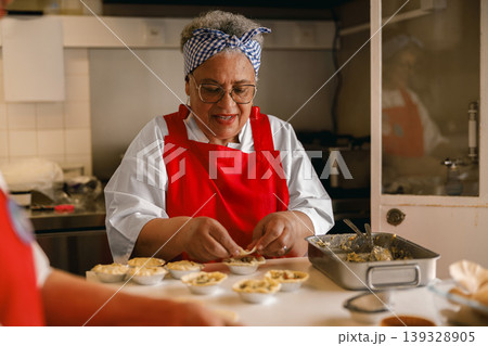 Senior Black Woman Chef Preparing Savory Pies in Professional Commercial Kitchen Setting 139328905