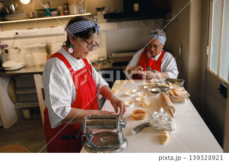 Senior Caucasian and Hispanic women baking pastries in a professional kitchen setting Senior Caucasian and Hispanic women baking pastries in a professional kitchen setting 139328921