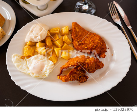 Tasty breaded pork cutlet with fried eggs and potatoes at plate Tasty breaded pork cutlet with fried eggs and potatoes at plate 139328970