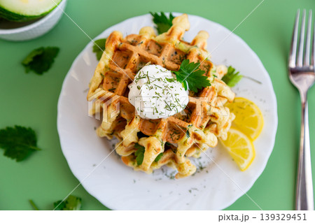 crispy zucchini waffles with sour cream and lemon slices on plate 139329451