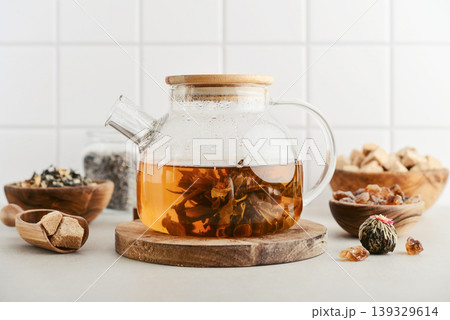 Blooming tea in a glass teapot with dry tea leaves, brown sugar in bowls, and ingredients on a light background. 139329614