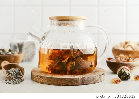 Blooming tea in a glass teapot with dry tea leaves, brown sugar in bowls, and ingredients on a light background. 139329615