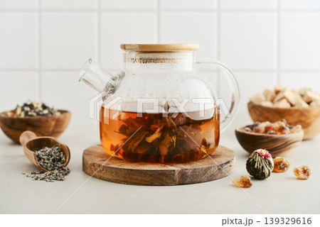 Blooming tea in a glass teapot with dry tea leaves, brown sugar in bowls, and ingredients on a light background. 139329616