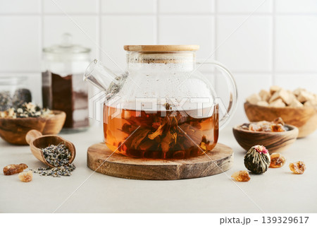 Blooming tea in a glass teapot with dry tea leaves, brown sugar in bowls, and ingredients on a light background. 139329617