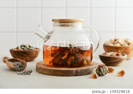 Blooming tea in a glass teapot with dry tea leaves, brown sugar in bowls, and ingredients on a light background. 139329618