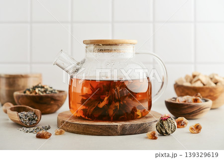 Blooming tea in a glass teapot with dry tea leaves, brown sugar in bowls, and ingredients on a light background. 139329619