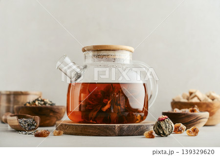 Blooming tea in a glass teapot with dry tea leaves, brown sugar in bowls, and ingredients on a light background. 139329620