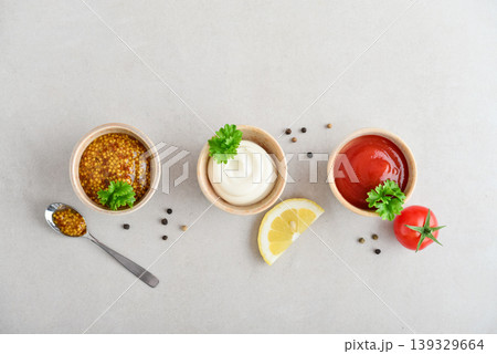 Top view of three small bowls with mayonnaise, ketchup, and mustard arranged in a row on a light background 139329664