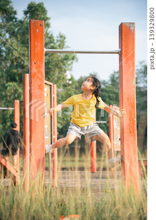 Young Girl Playing on Outdoor Gym Equipment in a Park, Engaging in Physical Activity and Enjoying Nature in Bright Yellow Shirt Young Girl Playing on Outdoor Gym Equipment in a Park, Engaging in Physical Activity and Enjoying Nature in Bright Yellow Shirt 139329800