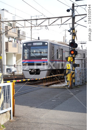 京成電車　踏切を通過するシルバーの車両と遮断機 139330544