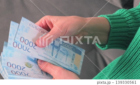 Female hands counting and organizing stacks of blue currency notes on a gray surface, showcasing the detailed design and denomination of the bills Female hands counting and organizing stacks of blue currency notes on a gray surface, showcasing the detailed design and denomination of the bills 139330561