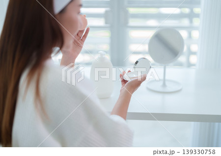 Asian women applying skincare product morning routine using mirror compact beauty cosmetic moisturizer face care treatment white bathrobe home bathroom hygiene Asian women applying skincare product morning routine using mirror compact beauty cosmetic moisturizer face care treatment white bathrobe home bathroom hygiene 139330758
