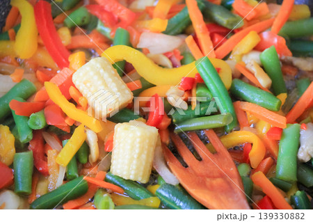 Cooking fresh colorful vegetable mix with baby corn and green beans using wooden spatula in a pan Cooking fresh colorful vegetable mix with baby corn and green beans using wooden spatula in a pan 139330882
