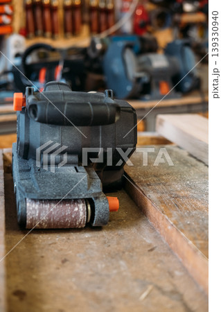 Carpentry equipment. Belt sander. Portable electric power joinery tool for professional work on wooden sawdust board in garage interior. Carpentry equipment. Belt sander. Portable electric power joinery tool for professional work on wooden sawdust board in garage interior. 139330940