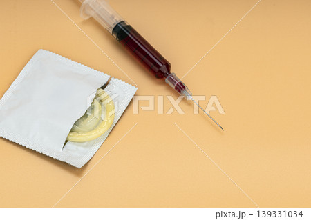 Open Condom Packet with Yellow Condom Beside a Blood-Filled Medical Syringe on Beige Background Representing Sexual Health, HIV Risk, and STI Prevention Concepts 139331034