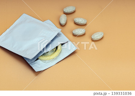 Open Condom Packets with Yellow Latex Condom and Scattered Beige Supplement Tablets on Warm Orange Background Representing Sexual Health and Safe Sex Awareness Open Condom Packets with Yellow Latex Condom and Scattered Beige Supplement Tablets on Warm Orange Background Representing Sexual Health and Safe Sex Awareness 139331036