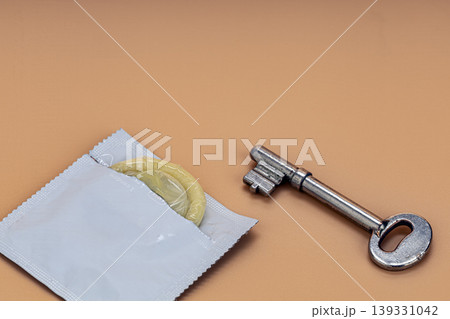 Open white condom packet revealing a yellow latex condom placed beside an antique silver skeleton key on a warm beige background, symbolizing safe sex and protection concepts Open white condom packet revealing a yellow latex condom placed beside an antique silver skeleton key on a warm beige background, symbolizing safe sex and protection concepts 139331042