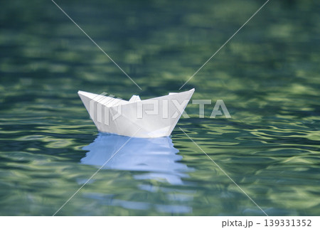 Close-up of simple small white origami paper boat floating quietly in blue clear river or sea water under bright summer sky. Freedom, dreams and fantasies concept, copyspace background. 139331352