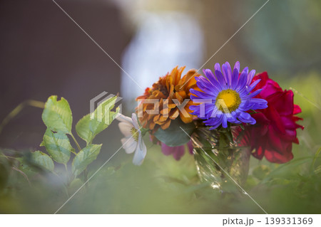 Close-up of beautiful autumn bright multicolored field flowers composition in transparent glass vase outdoors on blurred sunny bokeh copy space background. Postcard theme, beauty and fantasy concept. 139331369
