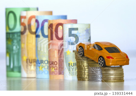 Blurred row of rolled hundred, fifty, twenty, ten and five new euro banknotes and pile of coins with yellow toy expensive sport car. Symbol of financial prosperity, vehicle sale and purchase. Blurred row of rolled hundred, fifty, twenty, ten and five new euro banknotes and pile of coins with yellow toy expensive sport car. Symbol of financial prosperity, vehicle sale and purchase. 139331444