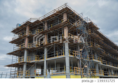 Multi-story building under construction with scaffolding against cloudy sky Multi-story building under construction with scaffolding against cloudy sky 139331725