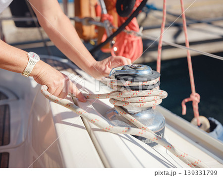 Detail view of hands working with nautical ropes and winches on sailing boat. Secure knotting and tension control are essential for safe mooring and sailing operations on yacht. Detail view of hands working with nautical ropes and winches on sailing boat. Secure knotting and tension control are essential for safe mooring and sailing operations on yacht. 139331799