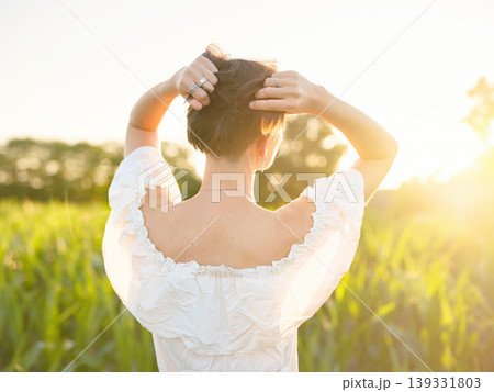 Beautiful woman in white dress standing in summer field during golden sunset in Croatia, warm sunlight, romantic evening mood, natural countryside atmosphere, soft wind and peaceful scene 139331803