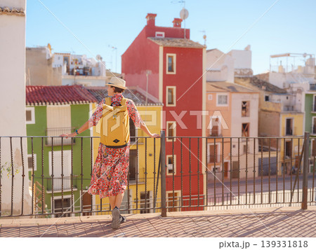 Woman in dress strolls through colorful streets of Spanish coastal town of La Vila Joiosa . sunny winter atmosphere highlights charm of Mediterranean architecture and quiet seaside life, back view Woman in dress strolls through colorful streets of Spanish coastal town of La Vila Joiosa . sunny winter atmosphere highlights charm of Mediterranean architecture and quiet seaside life, back view 139331818